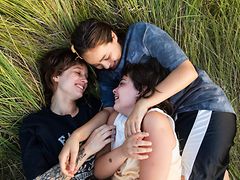  Drei junge Menschen liegen lachend gemeinsam im Gras.
