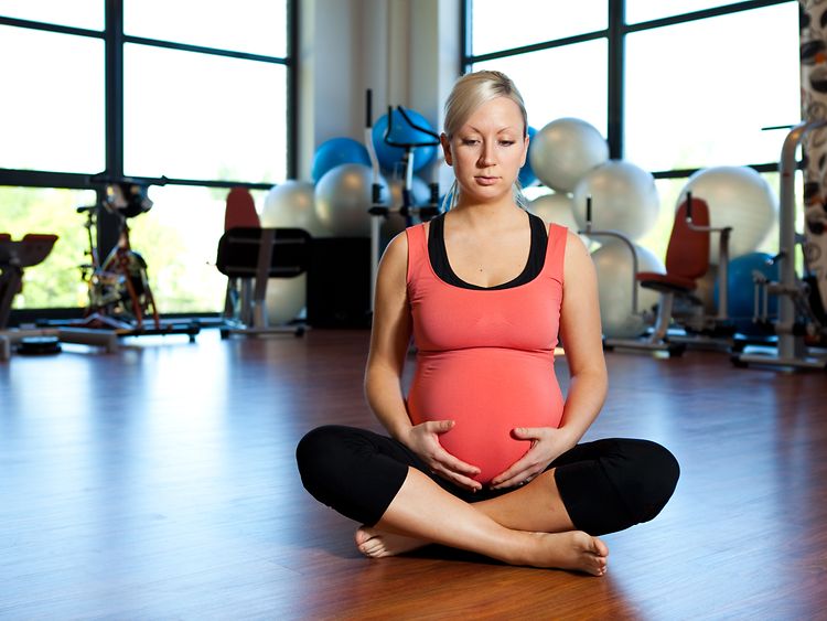  Eine schwangere Frau im Schneidersitz in einem Fit­ness-Stu­dio 