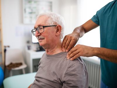  Ein Physiotherapeut behandelt den Nacken eines älteren Mannes