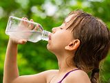  Ein Mädchen trinkt mit geschlossenen Augen Wasser aus einer Glasflasche.