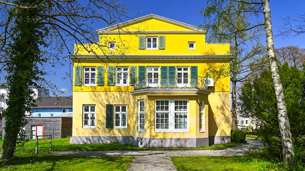 Historische gelbe Villa mit weißen Fensterrahmen und grünen Fensterladen