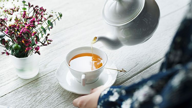  Person gießt Tee in Teetasse
