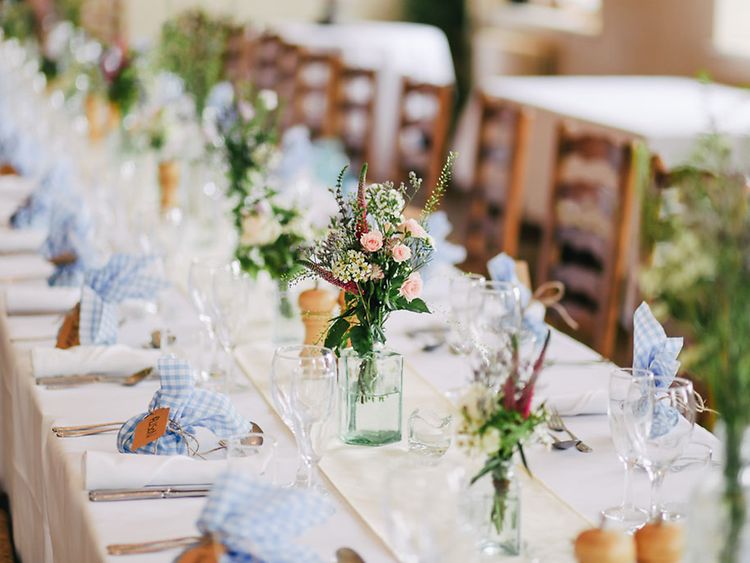  Eine gedeckte Tafel mit Blumen, Gläsern und blau-weiß-karierten Servietten.