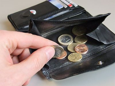  Hand greift in ein geöffnetes Kleingeldfach eines Portemonnaies mit wenigen Geldstücken