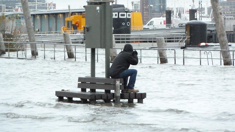  Die Elbe ist über ihre Ufer getreten. Auf einer Bank sitz ein Fotograf. Die Bank ist von Knie tiefem Wasser umspült.