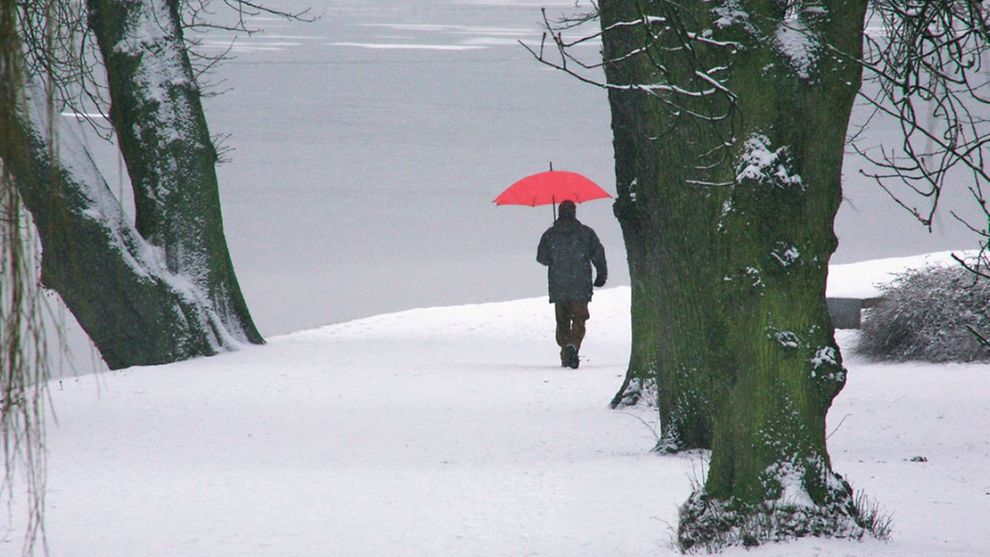 Mann mit Regenschirm geht durch Schneelandschaft