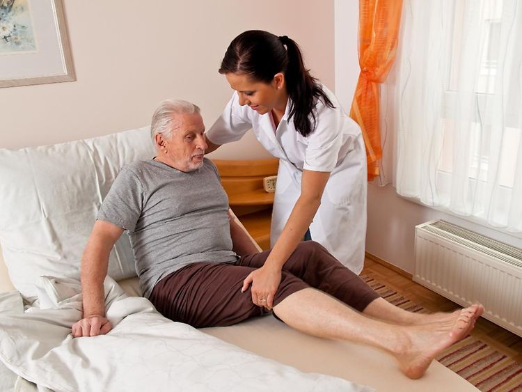  Eine Pflegerin hilft einem älteren Mann aus dem Bett