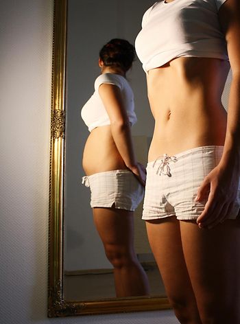 schlanke Frau sieht im Spiegel ein dickes Spiegelbild