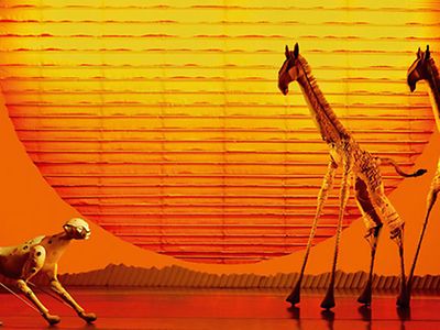  Darsteller stehen als Raubkatze und Giraffen inszeniert auf einer Bühne.