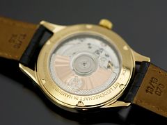  Eine Armbanduhr mit einem Lederband und einem goldenen Uhrrahmen. 