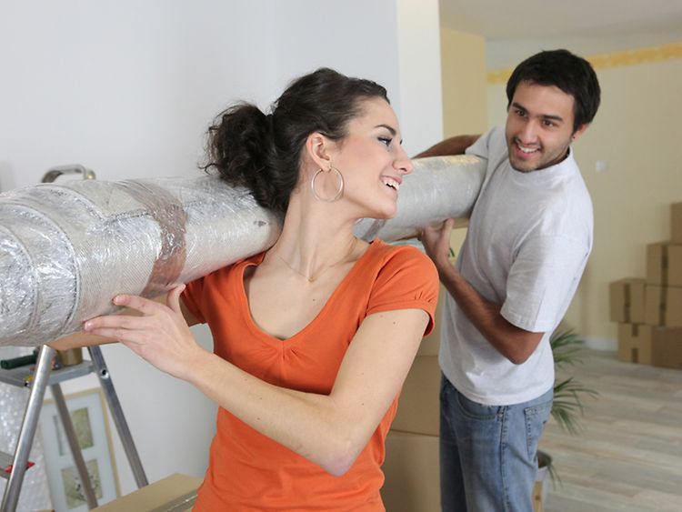  Frau und Mann tragen eine eingepackte Rolle durch eine unrenovierte Wohnung