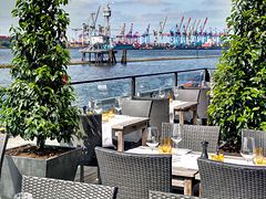  Die Terrasse des Au Quai mit Rattan Stühlen, gedeckten Tischen und Blick auf die Elbe.