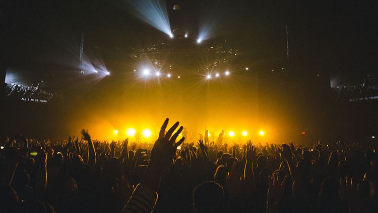  Publikum vor gelb erleuchteter Konzertbühne reckt die Hände in die Höhe