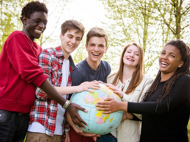  Junge Leute unterscheidlicher Hautfarbe halten eine Weltkugel