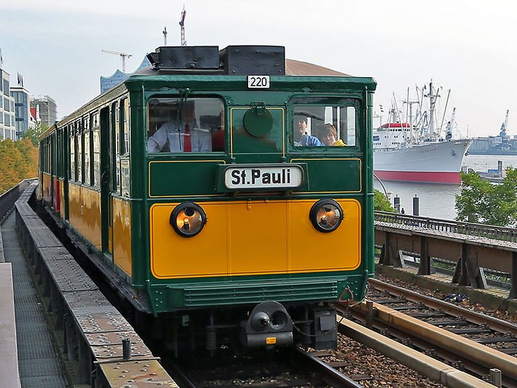 Eine historische Bahn in grün und gelb mit der Aufschrift "St. Pauli" fährt an den Landungsbrücken vorbei