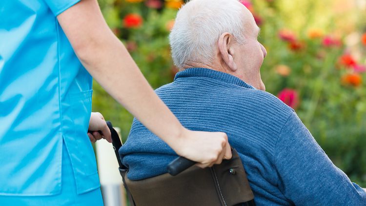  Senior im Rollstuhl wird von einer Pflegerin geschoben