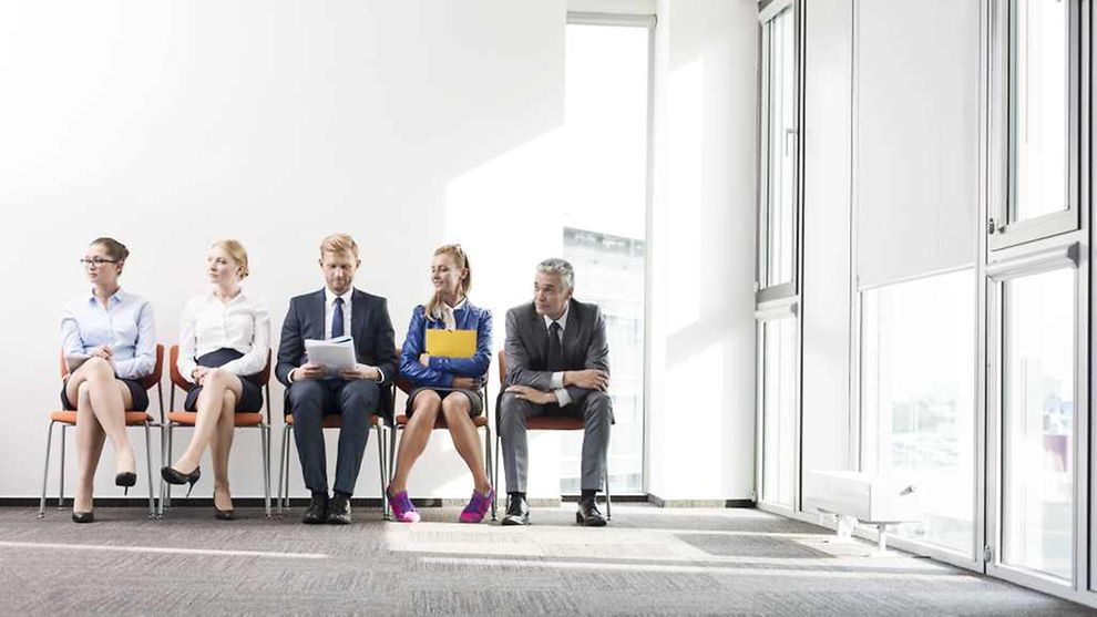 Frauen und Männer im Business-Outfit und mit Unterlagen sitzen in einer Reihe
