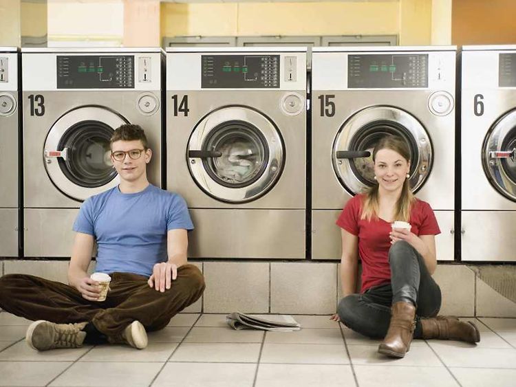  Junge Frau und junger Mann auf dem Boden sitzend vor Waschmaschinen in einem Waschsalon