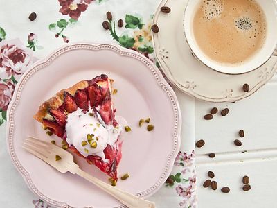  Ein Stück Zwetschgenkuchen auf einem rosa Teller und eine Tasse Kaffee daneben. 