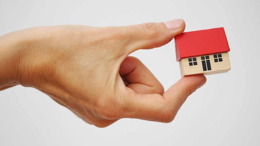 Zwei Finger halten ein kleines Haus-Modell 