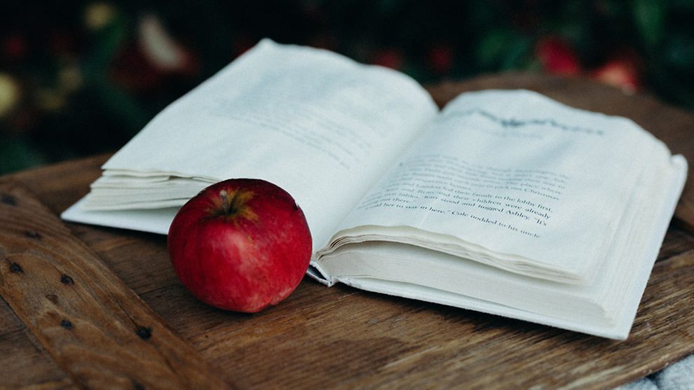 Ein roter Apfel liegt vor einem aufgeschlagenen Buch.