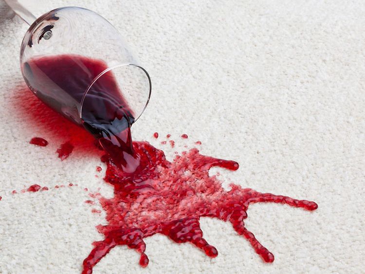  Ausgekipptes Glas Rotwein auf einem hellen Teppich