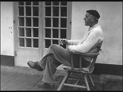  Mann mit Baskenmütze sitzt auf einem Stuhl vorm Haus