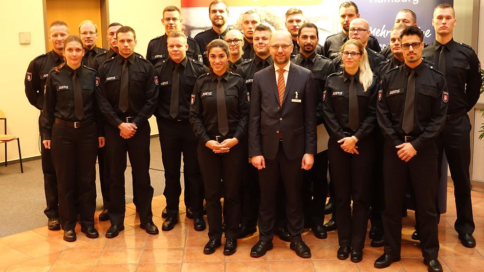 Junge Frauen und Männer in Uniformen des Justizvollzugs stehen in drei Reihen hintereinander, in der Mitte Justizsenator Dr. Steffen