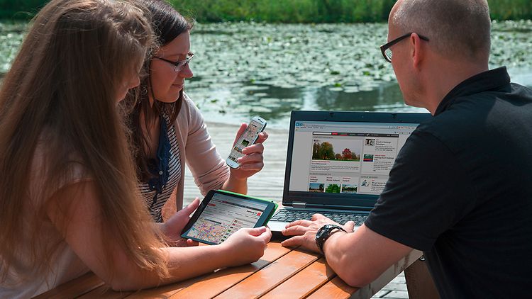  Menschen am See arbeiten mit Laptop, Tablet und Handy