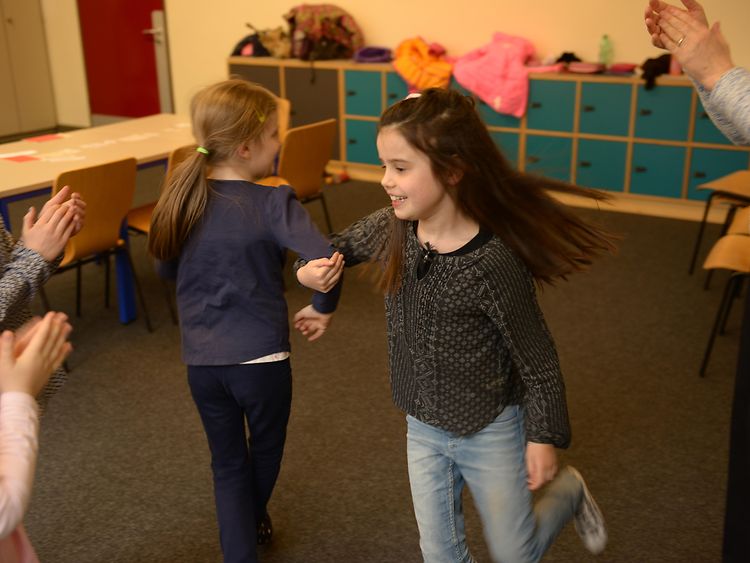  Solfège: Zwei Kinder tanzen ausgelassen, die anderen klatschen dazu im Kreis.