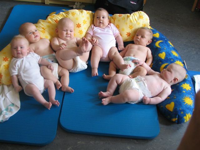 Sechs Babys liegen nebeneinander auf Matten und Kissen