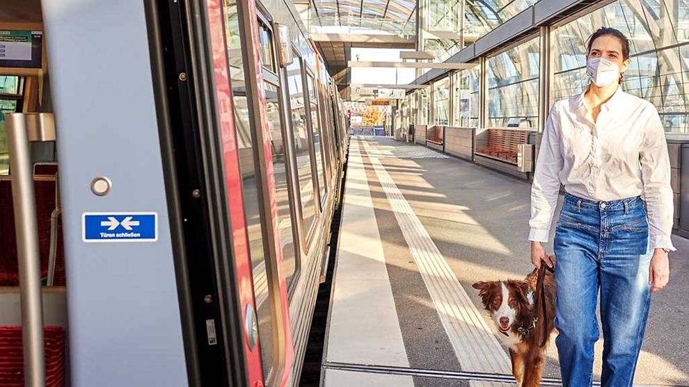  Eine Frau mit Mund-Nasen-Bedeckung und einem Hund geht in Richtung einer stehenden U-Bahn.