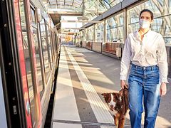  Eine Frau mit Mund-Nasen-Bedeckung und einem Hund geht in Richtung einer stehenden U-Bahn.
