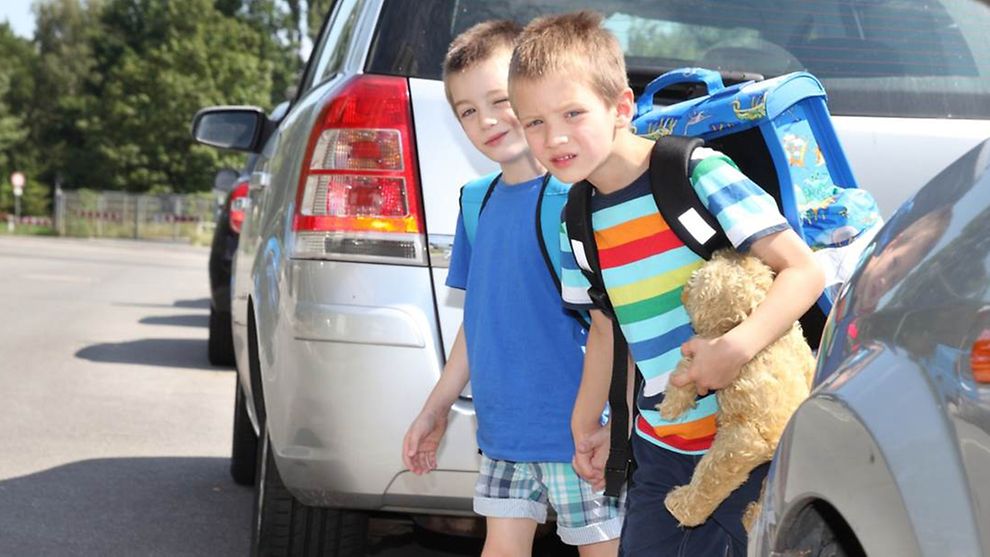 Zwei Schulkinder zwischen parkenden Autos