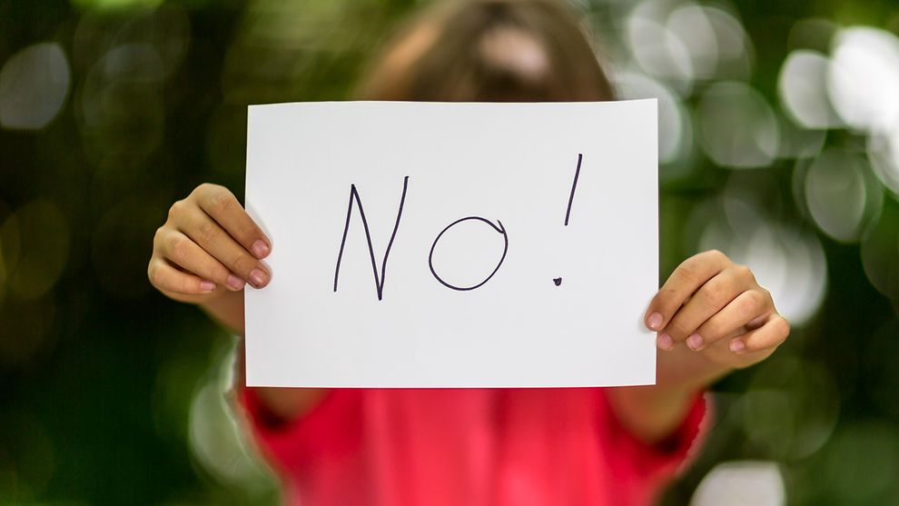 Ein schemenhaft dargestelltes Mädchen hält einen großen weißen Zettel mit der Aufschrift "No!" so vor sich, dass es selbst kaum zu sehen ist.