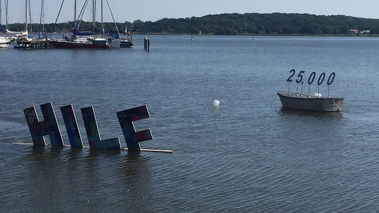  Das Kunstprojekt auf der Schlei zeigt die Buchstaben HILF im Wasser stehend und ein Boot mit der Zahl 25000